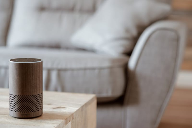 Modern living-room scene with a smart speaker, smart lighting and a phone showing a home-control app — illustrating a typical smart home setup